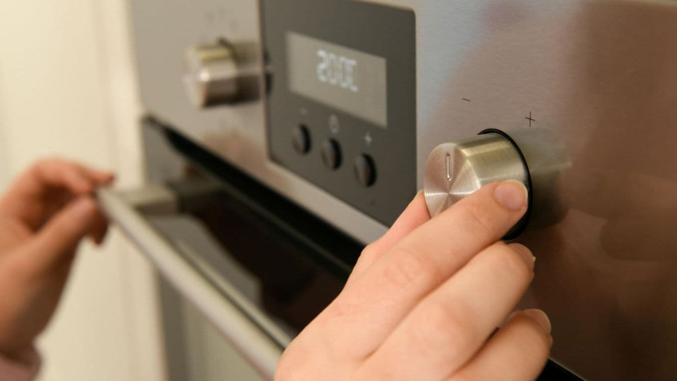 Person Adjusting Temperature Knob On Oven