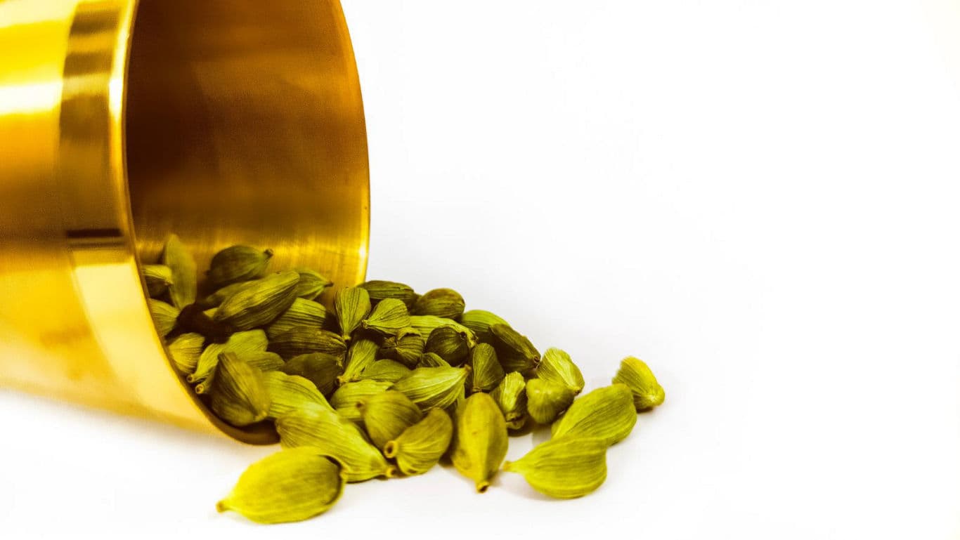 Green cardamom pods spilling from golden container
