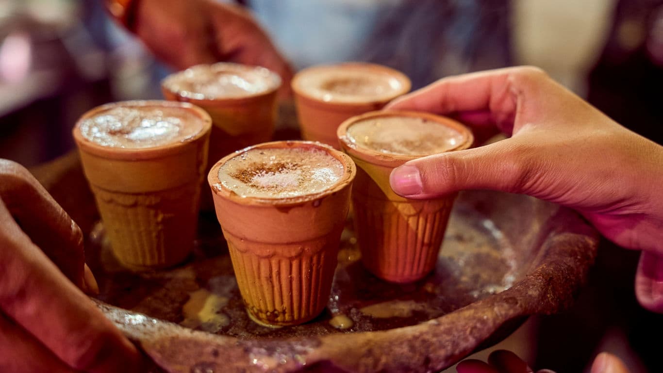 Hands sharing traditional clay cups of chai