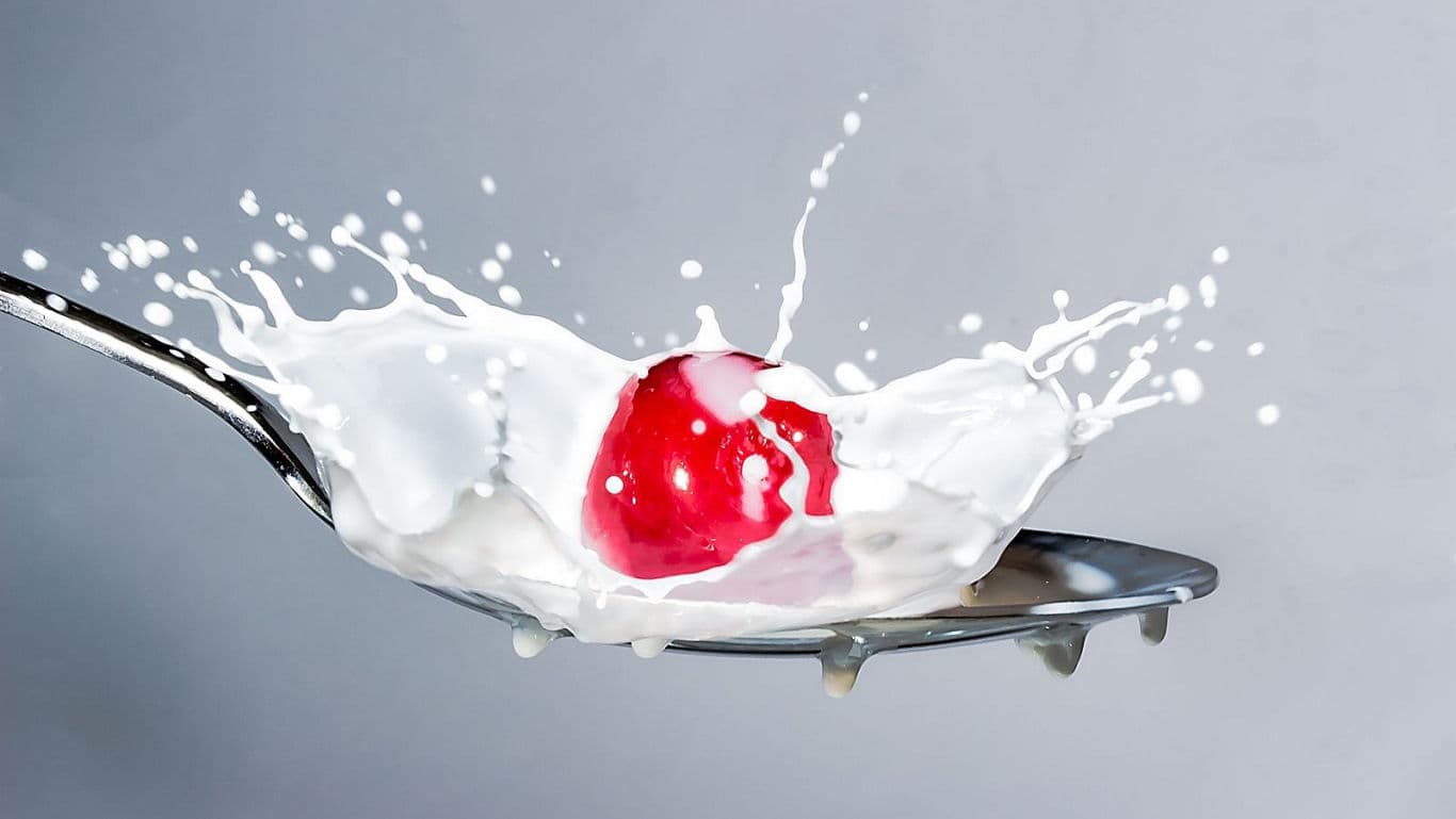 Red cherry splashing into spoonful of milk