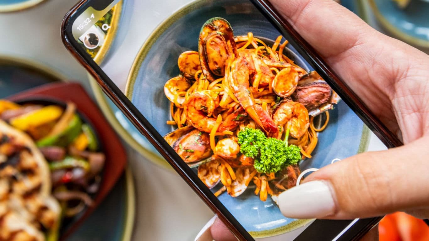 Person photographing seafood pasta dish on phone