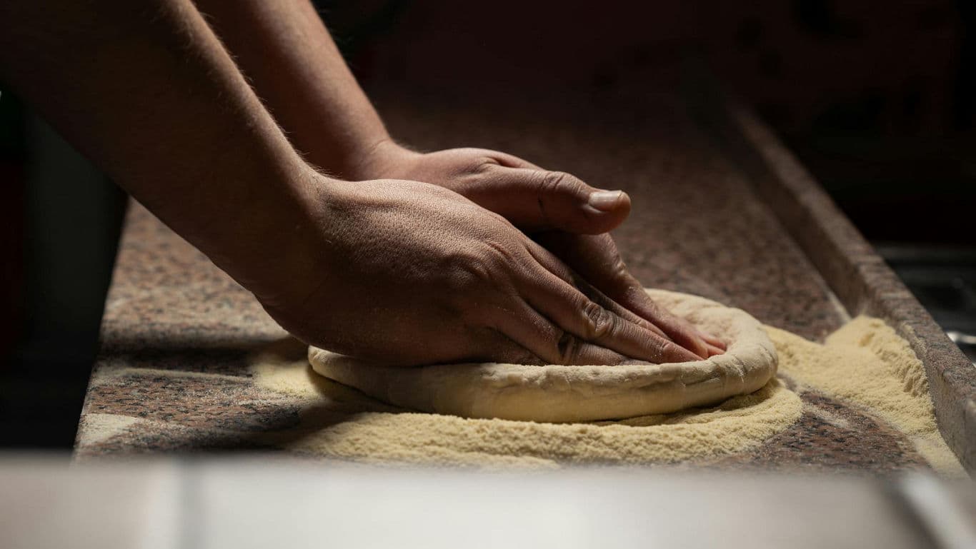 Hands Shaping Pizza Dough on Floured Surface