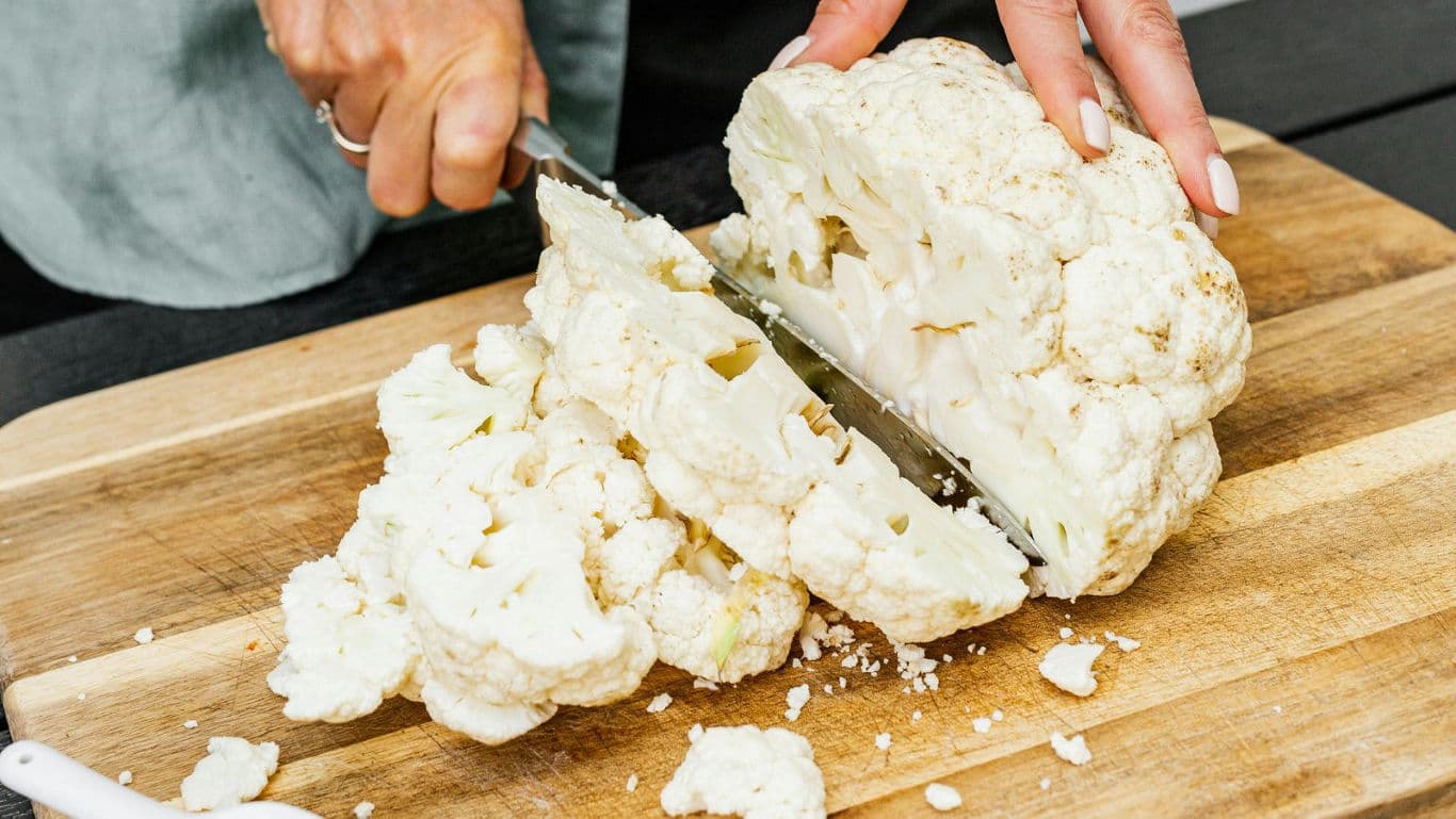 Person slicing fresh cauliflower on board