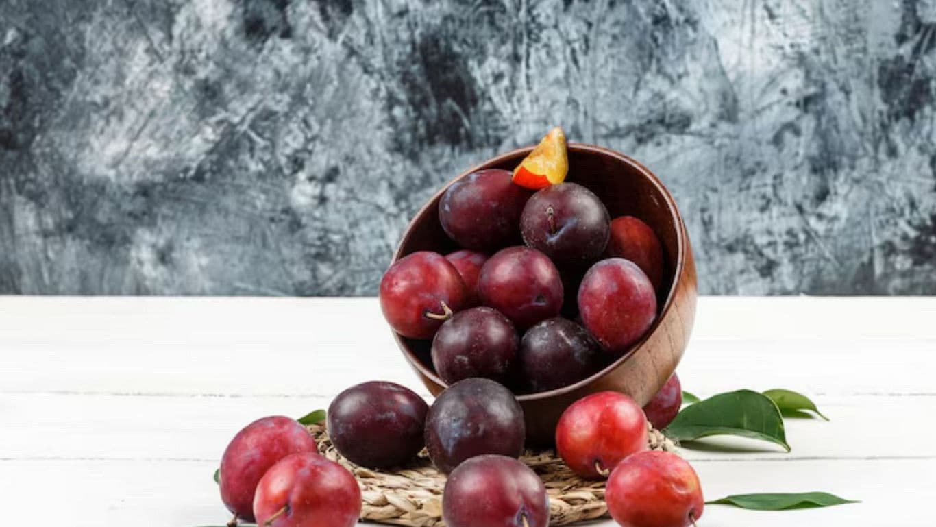 Fresh ripe plums in wooden bowl on table