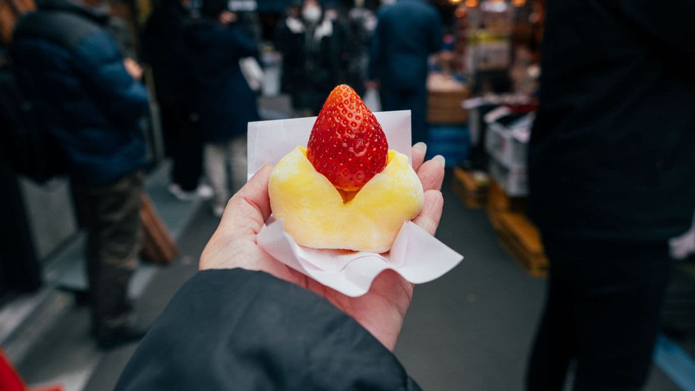 Hand holding strawberry dessert in street market