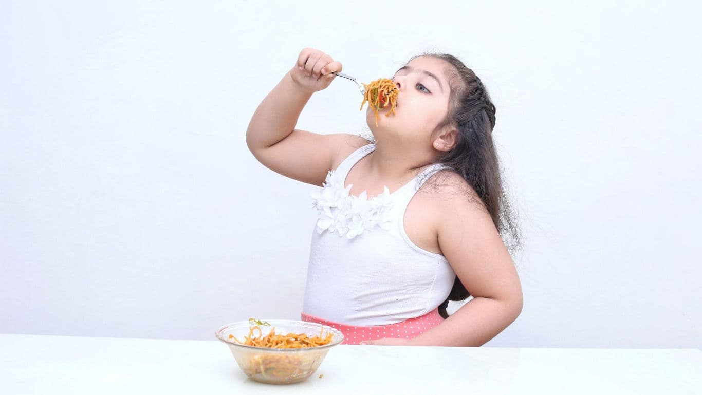 Young girl eating noodles at table