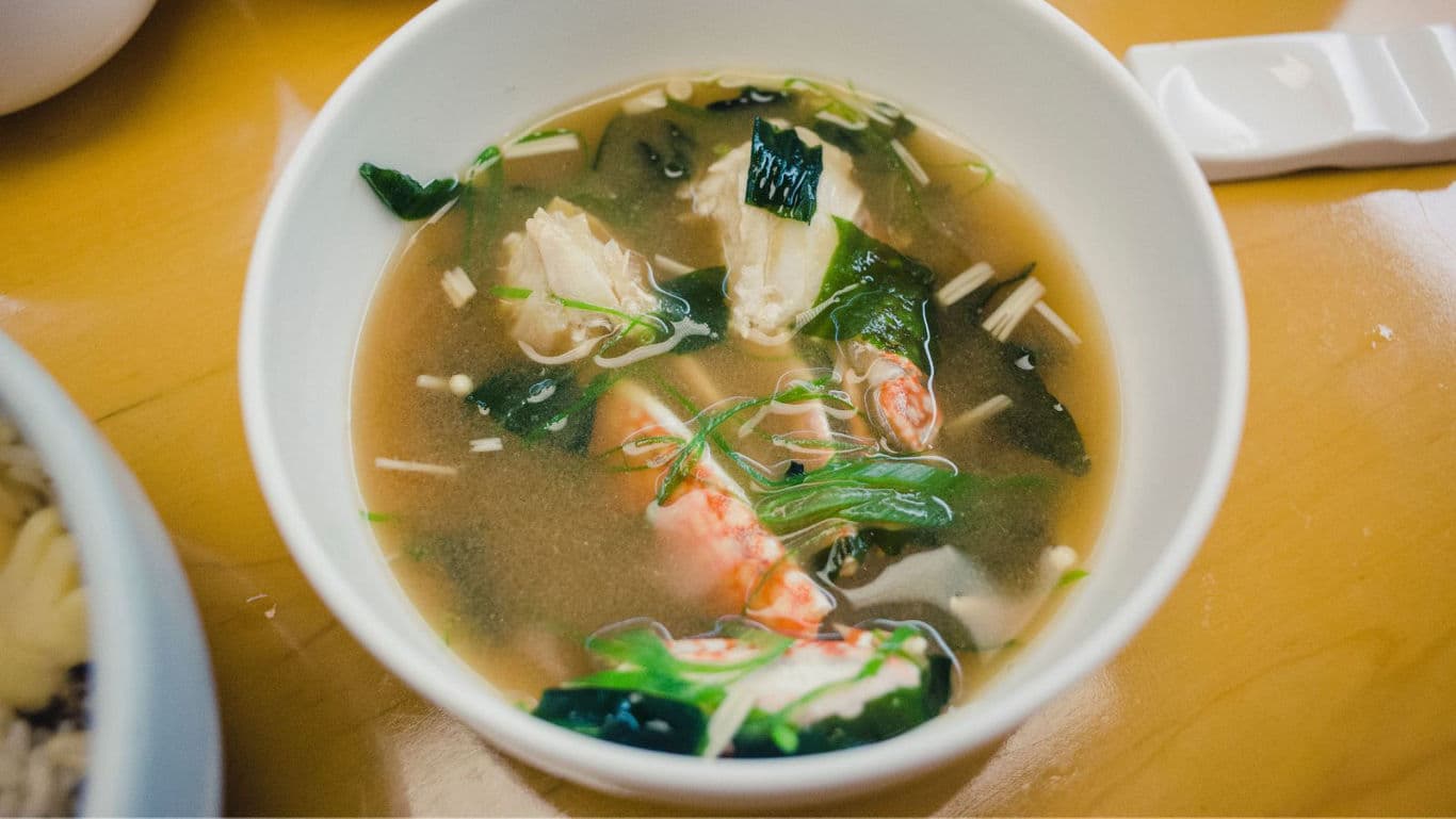 Seafood soup with greens in white bowl