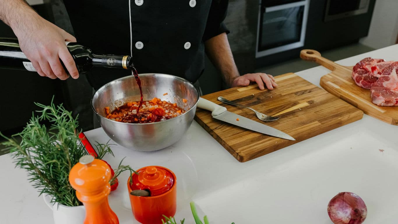 Chef pouring wine into stainless mixing bowl