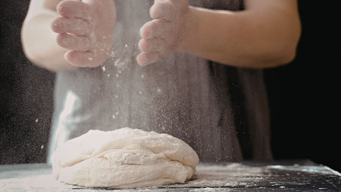 Hands dusting flour over fresh bread dough