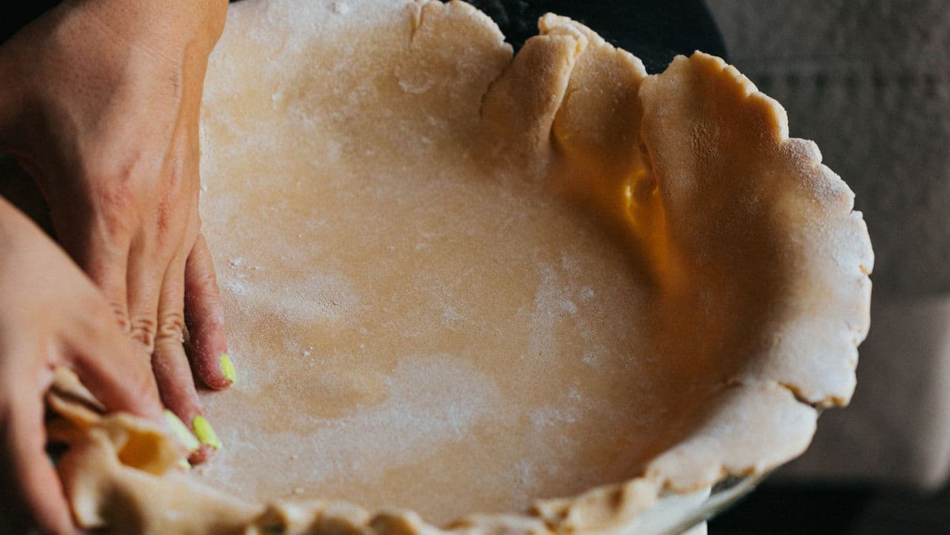 Hands pressing homemade pie crust into dish