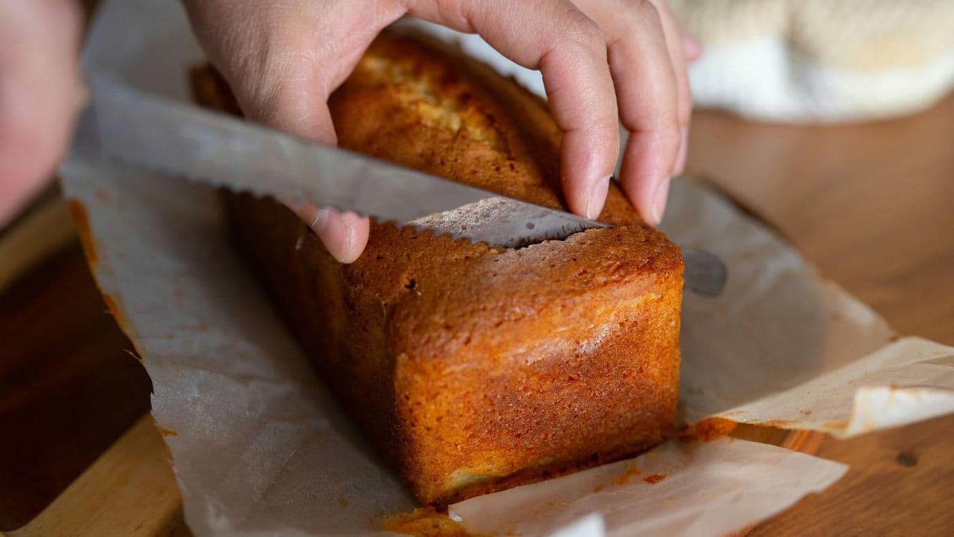 Hands slicing freshly baked loaf cake