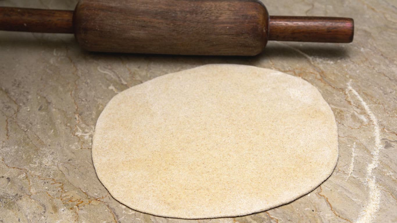 Rolled dough with wooden rolling pin on countertop
