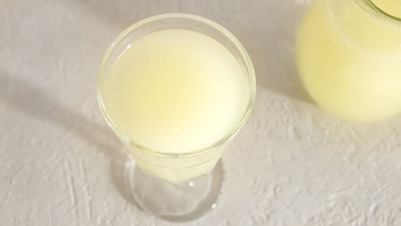 Glass of pale yellow beverage on white surface