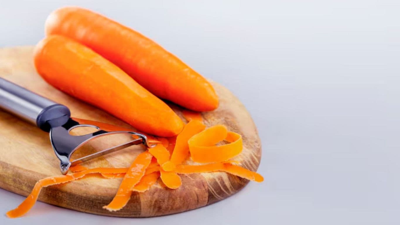 Fresh carrots and peeler on wooden cutting board