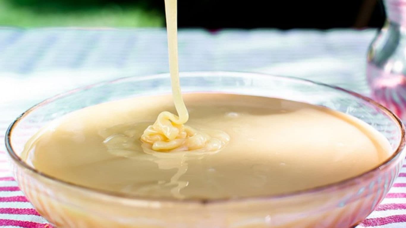 Sweet condensed milk pouring into glass bowl