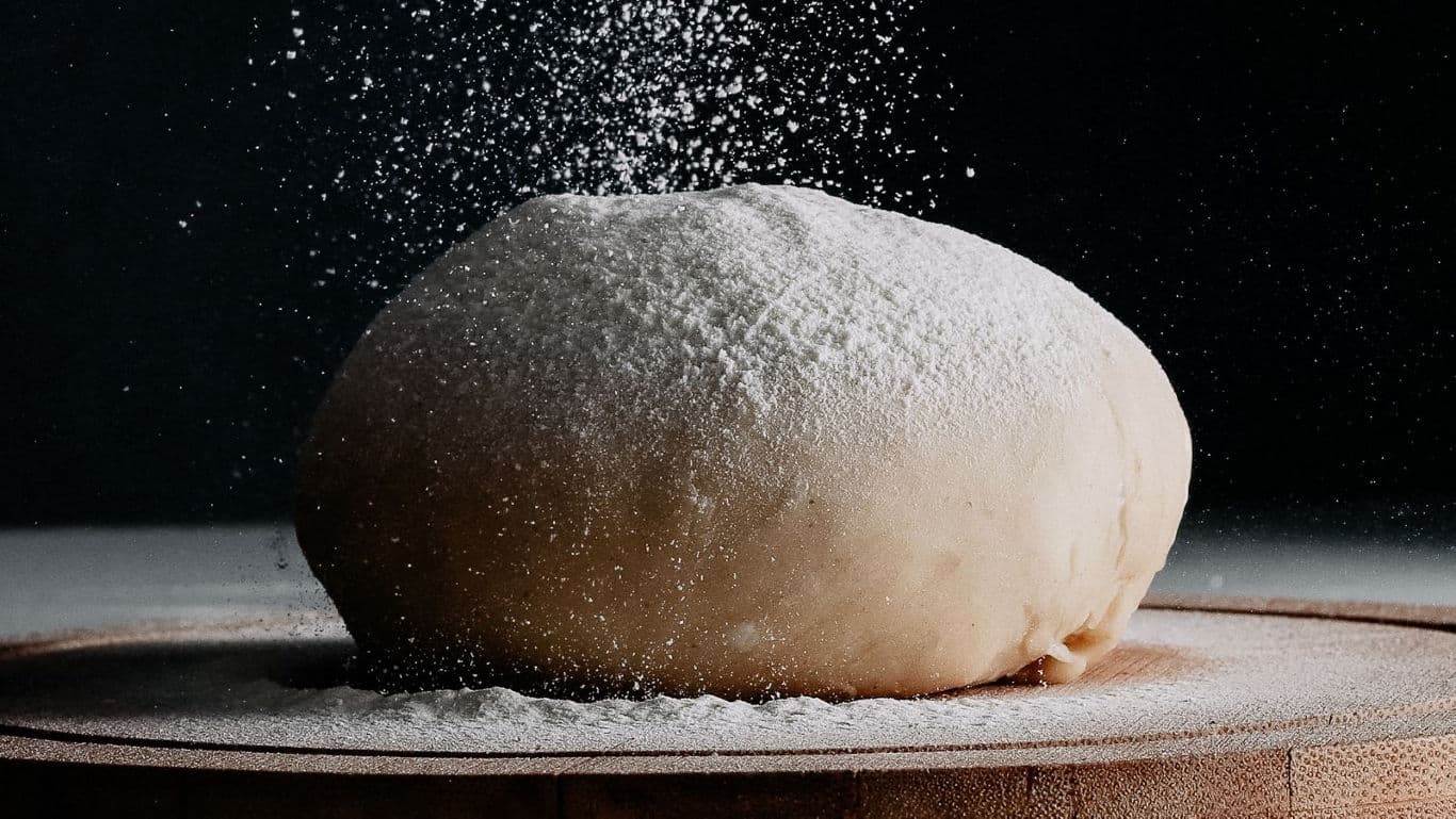 Fresh dough ball dusted with flour on board
