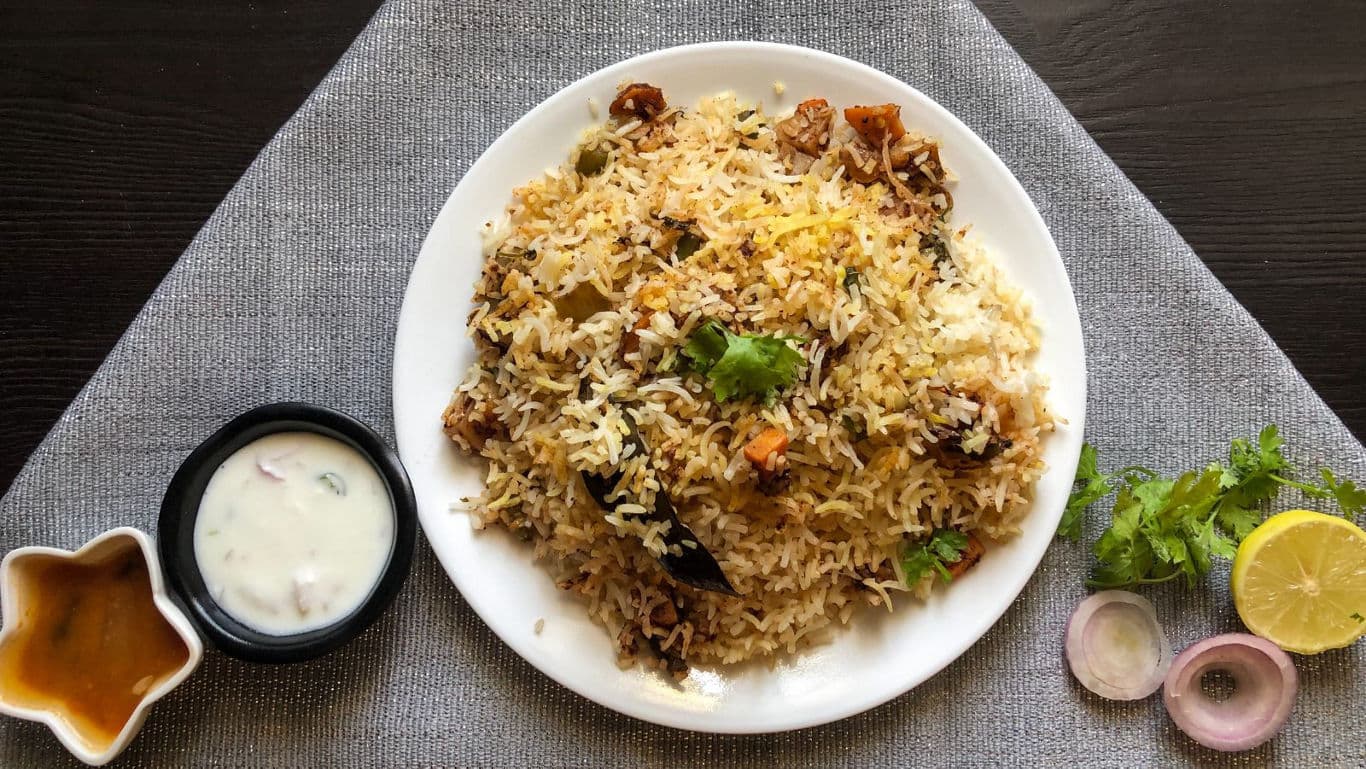 Plate of biryani rice with raita and chutney sides