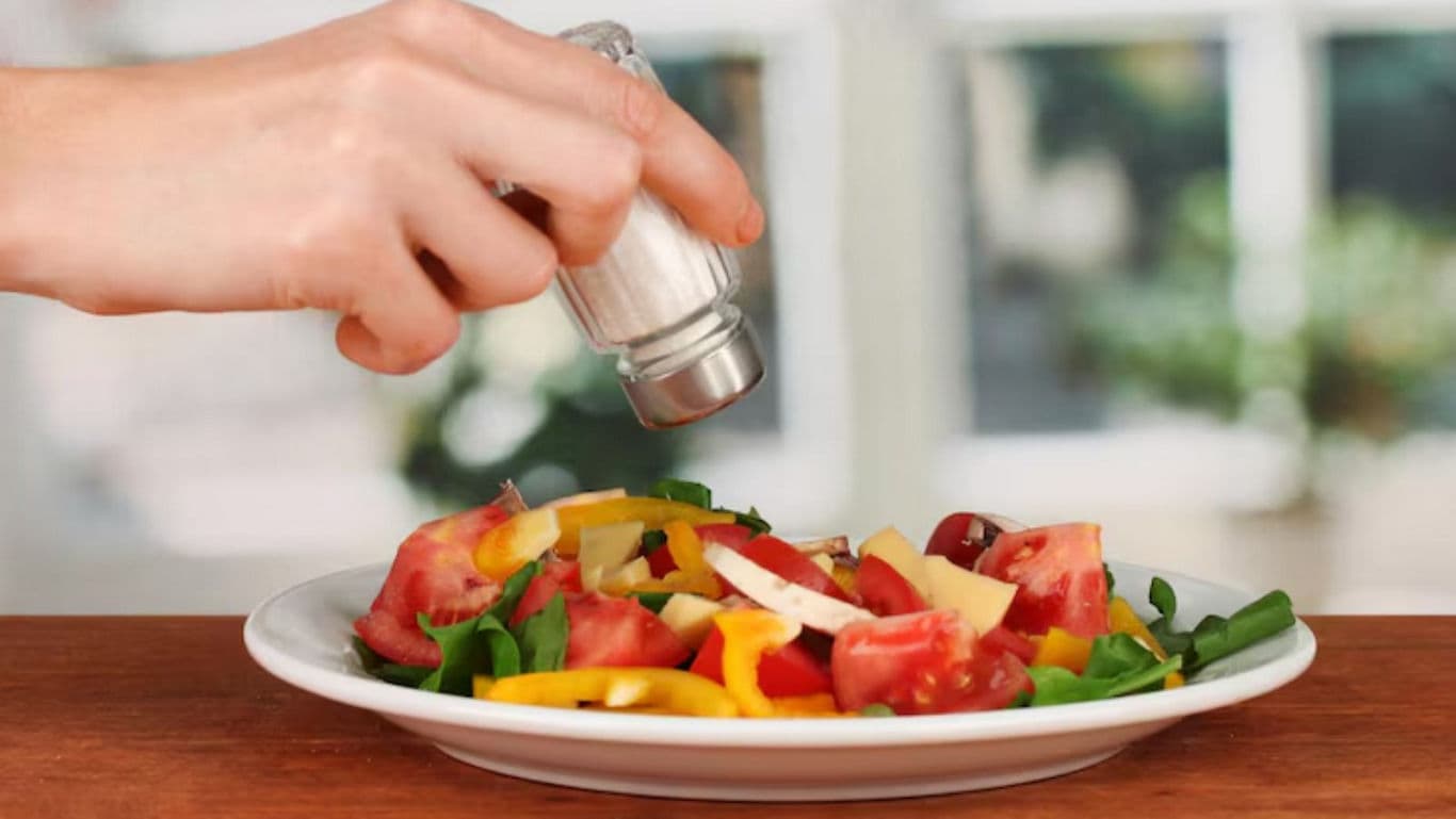 Hand Sprinkling Salt on Fresh Vegetable Salad