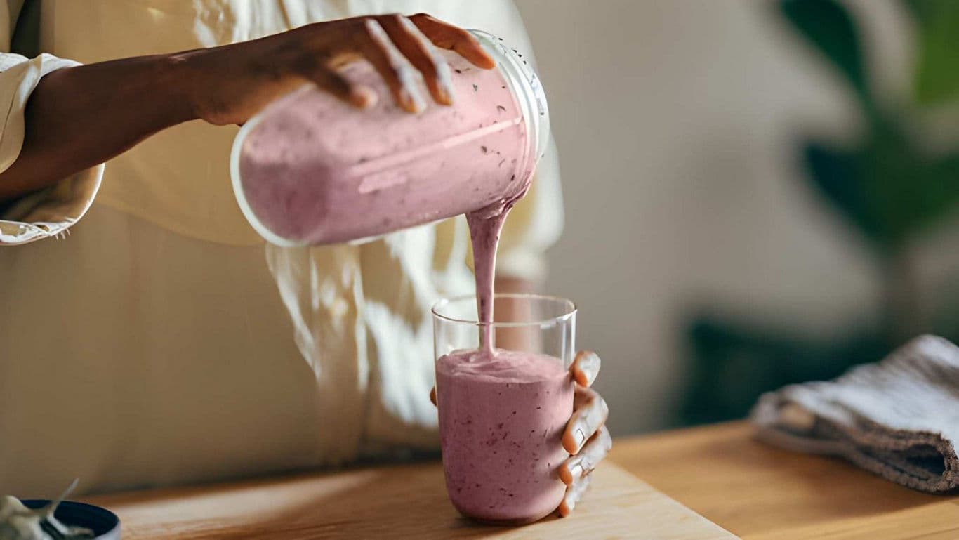 Person Pouring Fresh Berry Smoothie Into Glass