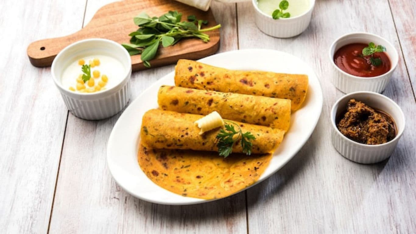 Methi thepla served on a white plate with curd and pickle on the side.