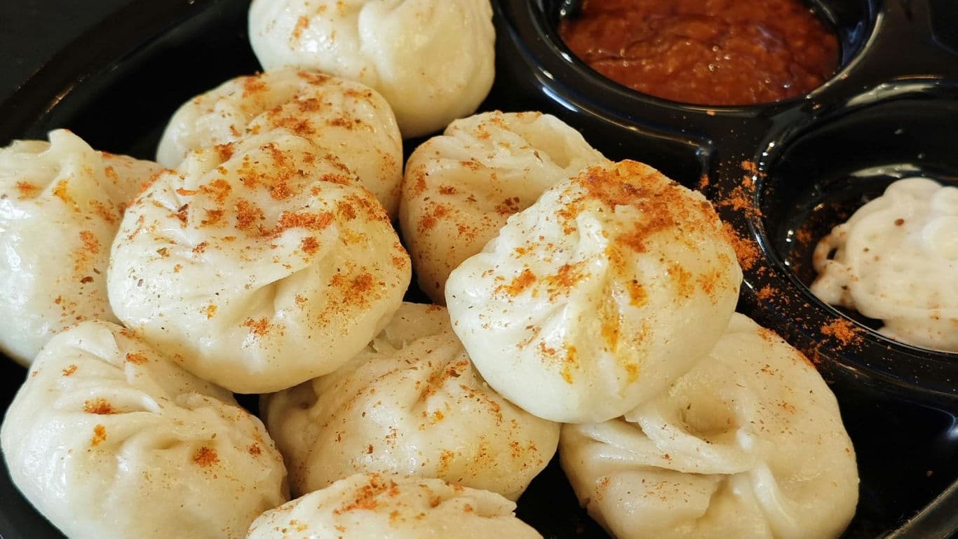 Plate of steamed paneer momos served in traditional wooden boxes